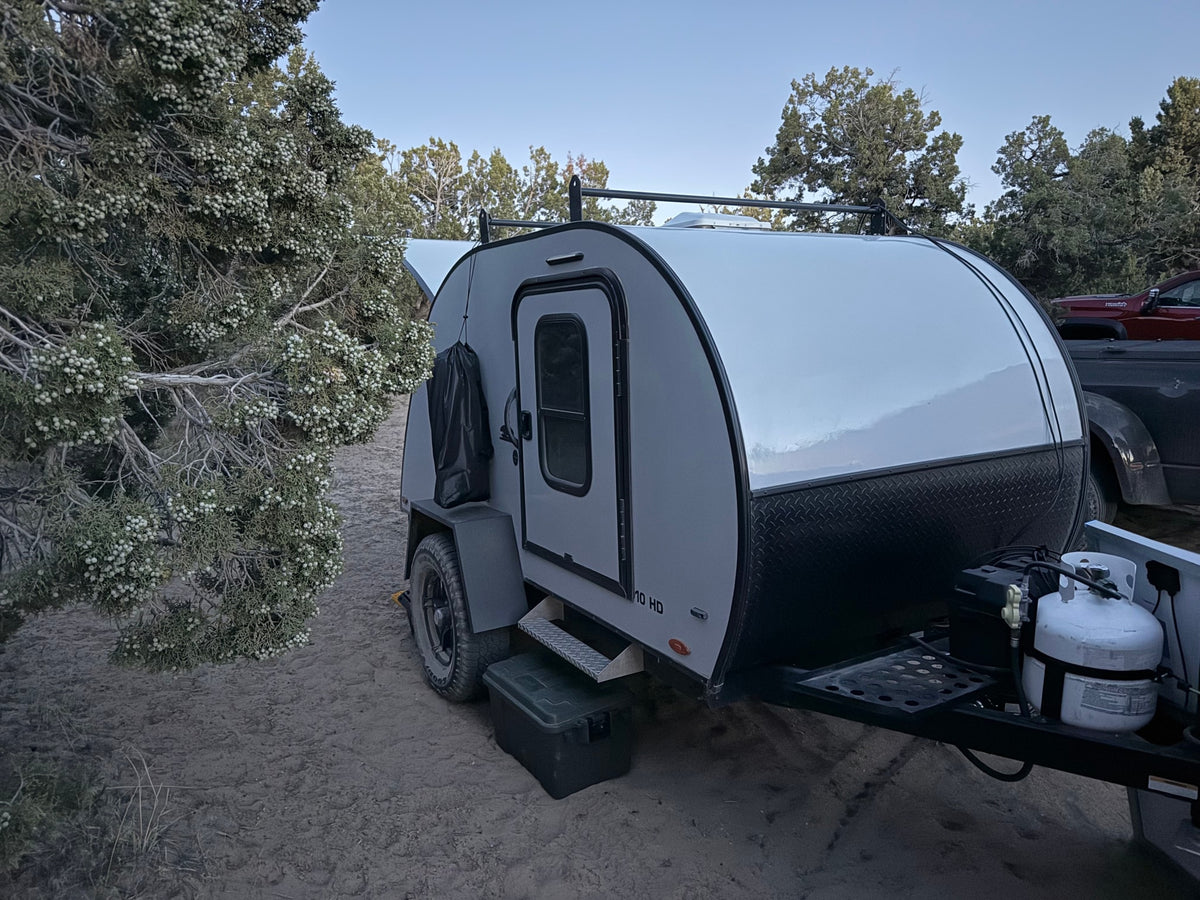 This rugged RV rental, a compact teardrop camper, sits on sandy ground by a berry-laden juniper tree. — photo 7