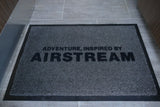 Inside an RV rental, a grey Airstream welcome mat reads 'ADVENTURE, INSPIRED BY AIRSTREAM' on a tiled floor.
