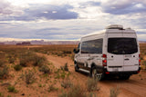This white RV rental, a camper van, explores a desert dirt road. Ideal for scenic off-road adventures and memorable road trips.