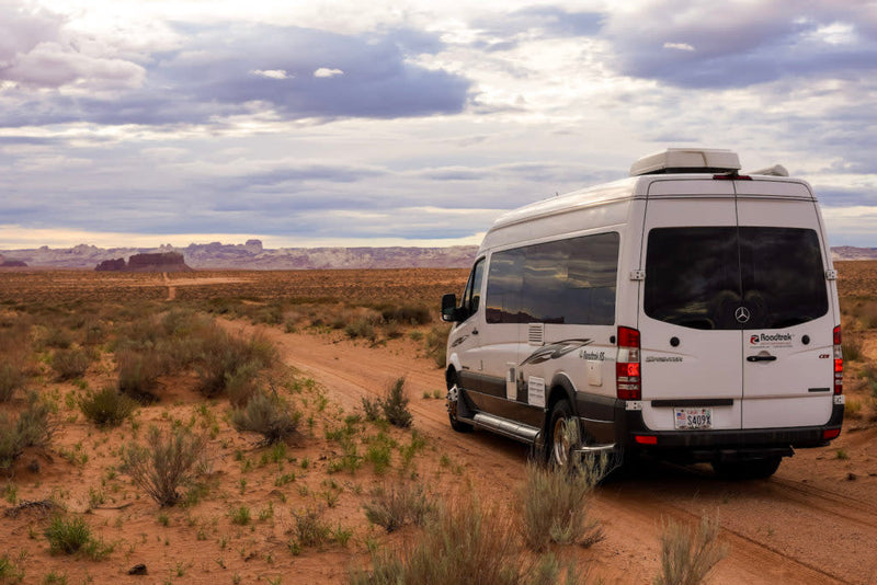  showcasing stunning red and white desert mountains under a blue sky.|Roadtrek RV rental van by a massive rock spire in a desert landscape — photo 9