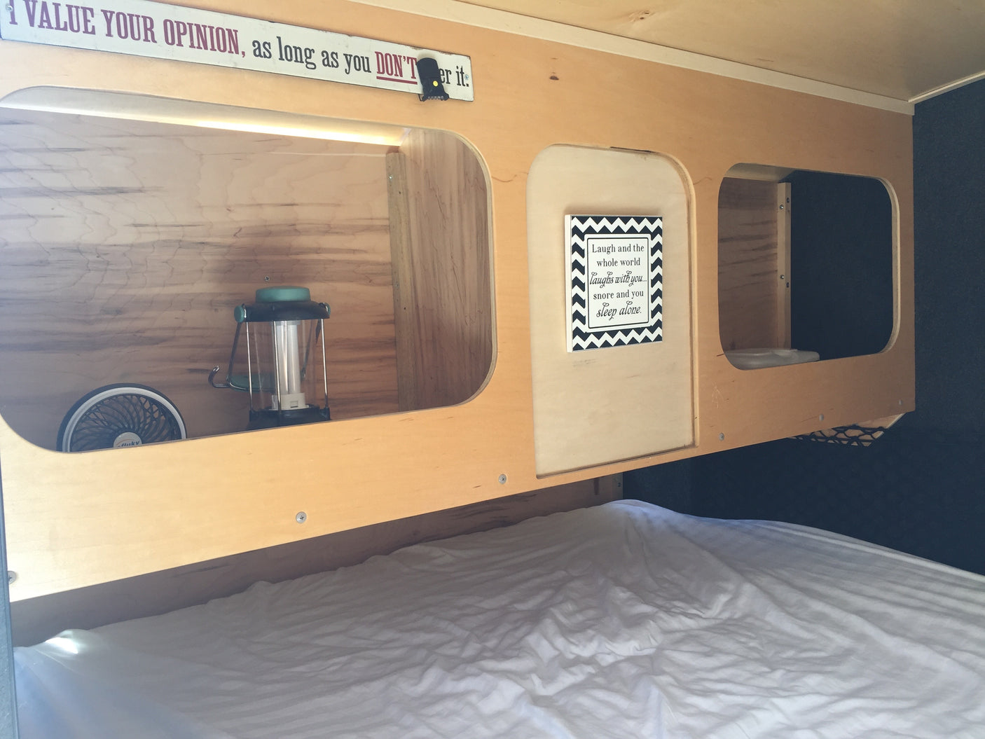 Cozy rv rental bed area featuring wooden cubbies with a fan, lantern, and whimsical signs. Perfect for compact travel.