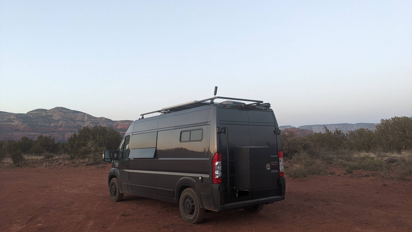 Dark grey adventure van, ideal rv rental, on red desert earth with mountains at dusk.