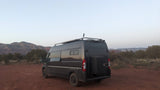 Dark grey adventure van, ideal rv rental, on red desert earth with mountains at dusk.