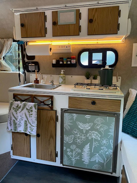 Modern RV rental kitchen setup with sink, stove, & a unique botanical-themed fridge. Organized & inviting space. — photo 3
