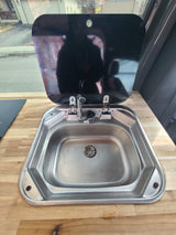 Compact stainless steel sink with folding faucet in an RV rental, featuring a sleek wooden countertop.