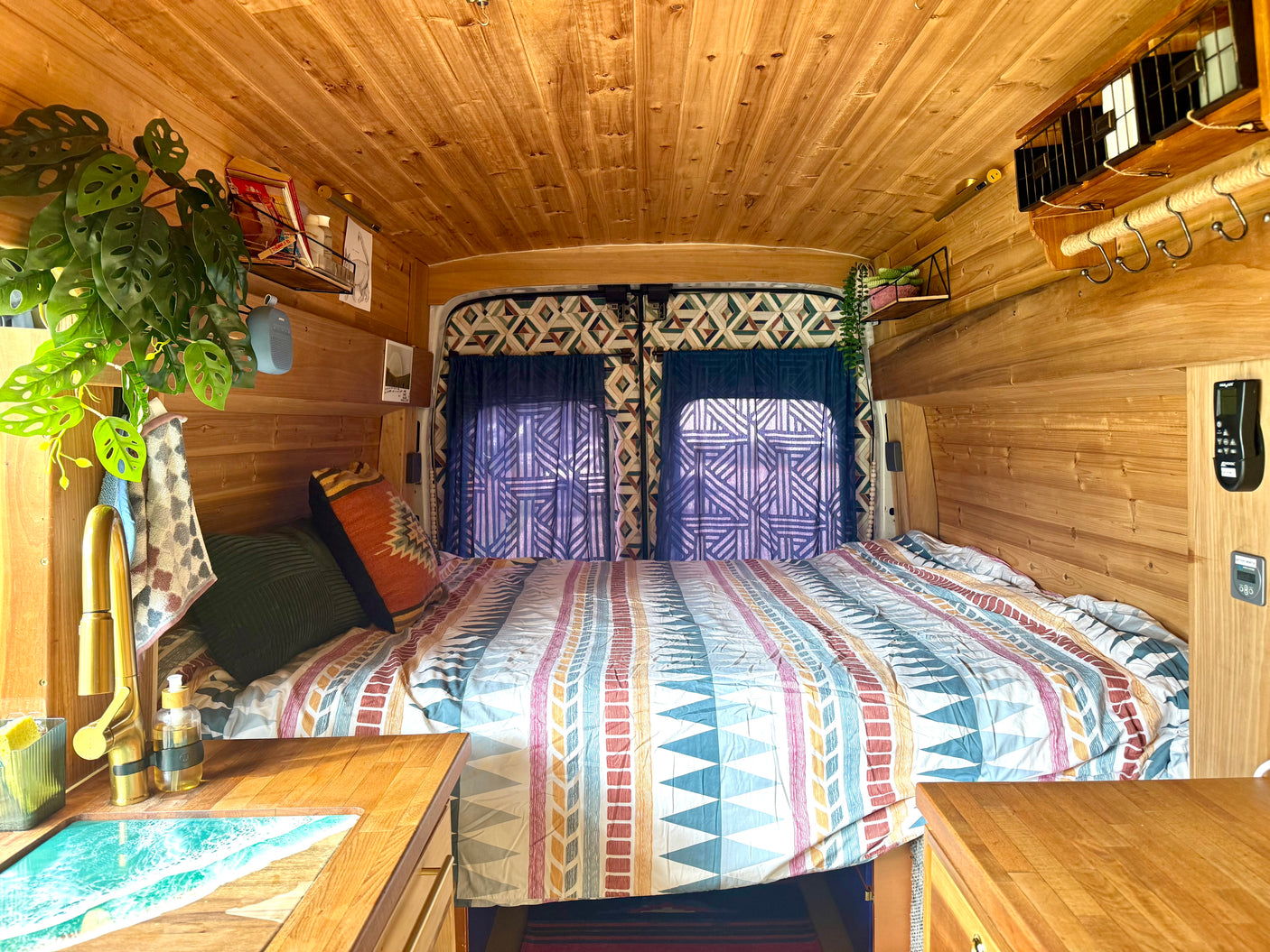 Warm wood-paneled RV rental interior: a cozy bed, unique ocean-themed sink, and vibrant decor for a comfortable journey.