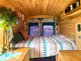 Warm wood-paneled RV rental interior: a cozy bed, unique ocean-themed sink, and vibrant decor for a comfortable journey.