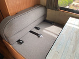 Comfortable grey dinette seating with visible seatbelts in an RV rental interior, by a window.