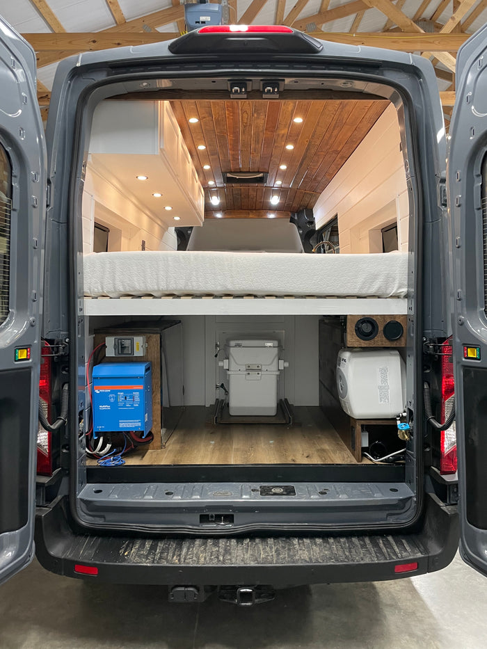 Inside this custom gray camper van RV rental: a comfortable bed, Victron power system, slide-out toilet, and water heater.