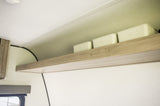 RV rental cabin interior features a light wood shelf with three pale storage bins. Above are curved light-colored panels.