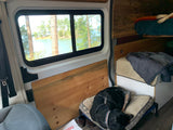 Cozy RV rental interior: dog sleeps on bed, window frames serene lake, pine trees. Perfect for pet-friendly travel.