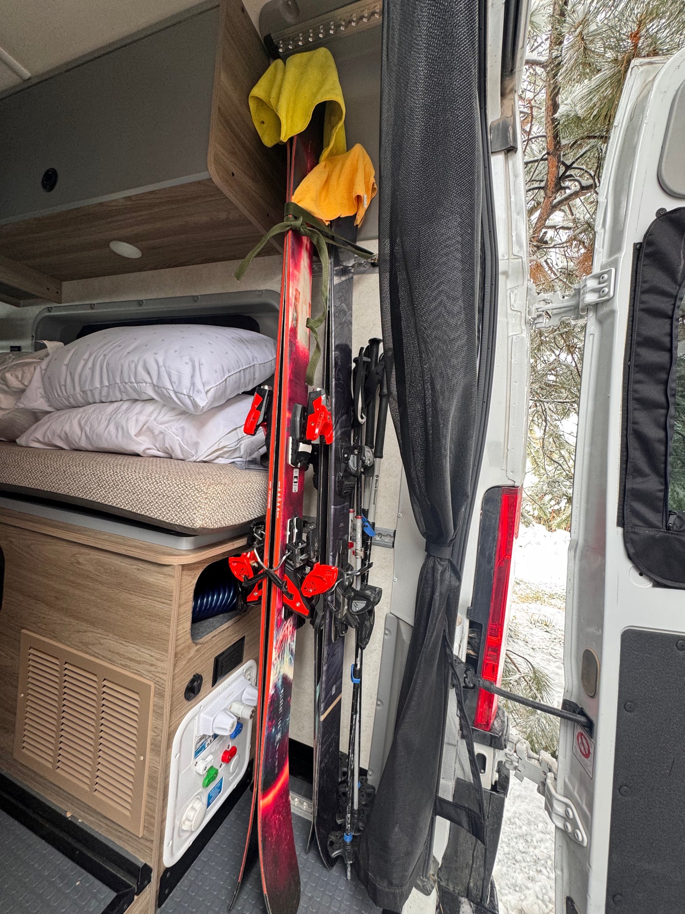 RV rental interior: Skis, poles, & bedding neatly stored in a camper van for a winter adventure, with snowy trees visible outside.