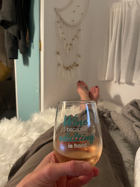 Cozy RV rental evening. Relaxing with feet up, holding a wine glass that reads "adulting is hard."