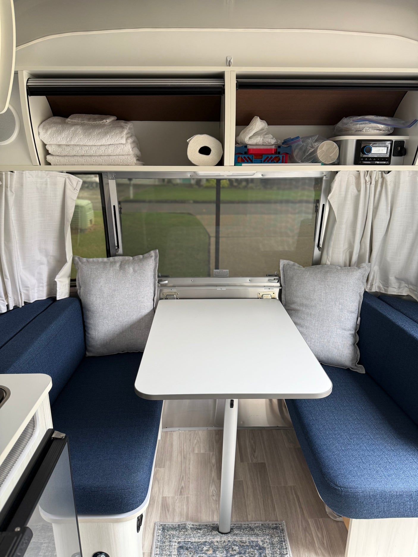 Inside this modern RV rental: blue seating, a white dining table, and functional overhead storage with towels & tech.