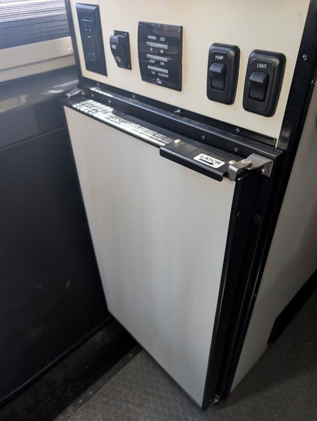 RV rental interior: control panel with pump/light switches, awning LED controls, power outlet, and cabinet latch.