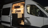 Bright, modern camper van interior with open door, showing kitchen and wooden accents. Ideal for rv rental.