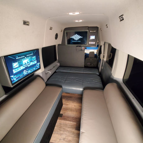 Spacious RV rental interior with convertible seating, two TVs, and wood flooring for comfort and entertainment.