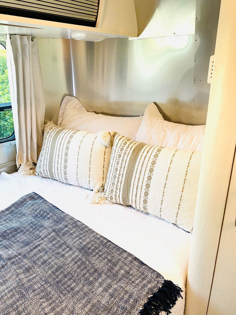 Cozy RV rental bedroom featuring a comfortable bed with decorative pillows, white bedding, and a dark throw blanket.
