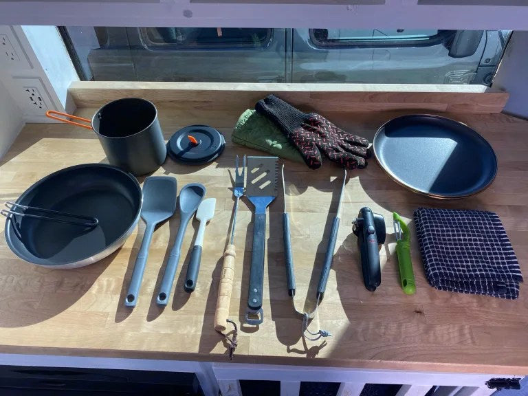 RV rental kitchen essentials: Pot, pan, grill tools, cooking utensils, gloves, and a plate arranged on a light wood counter. — photo 2