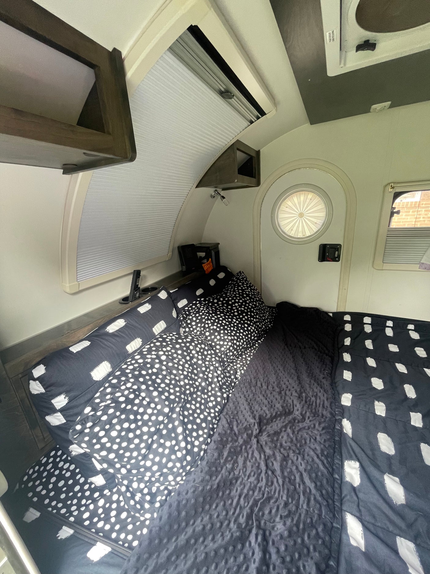 Cozy rv rental bedroom showing a bed with black and white polka dot and brushstroke patterned bedding and windows.