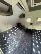 Cozy rv rental bedroom showing a bed with black and white polka dot and brushstroke patterned bedding and windows.