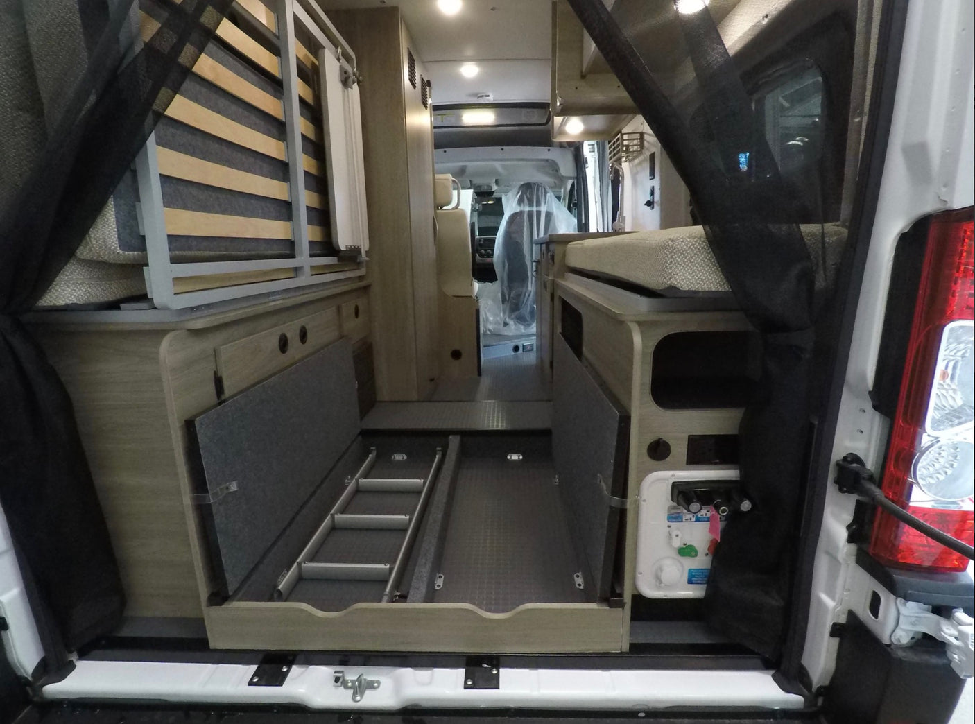 Explore this RV rental's versatile camper van interior: rear view shows a convertible bed, pull-out storage, and utility panel.