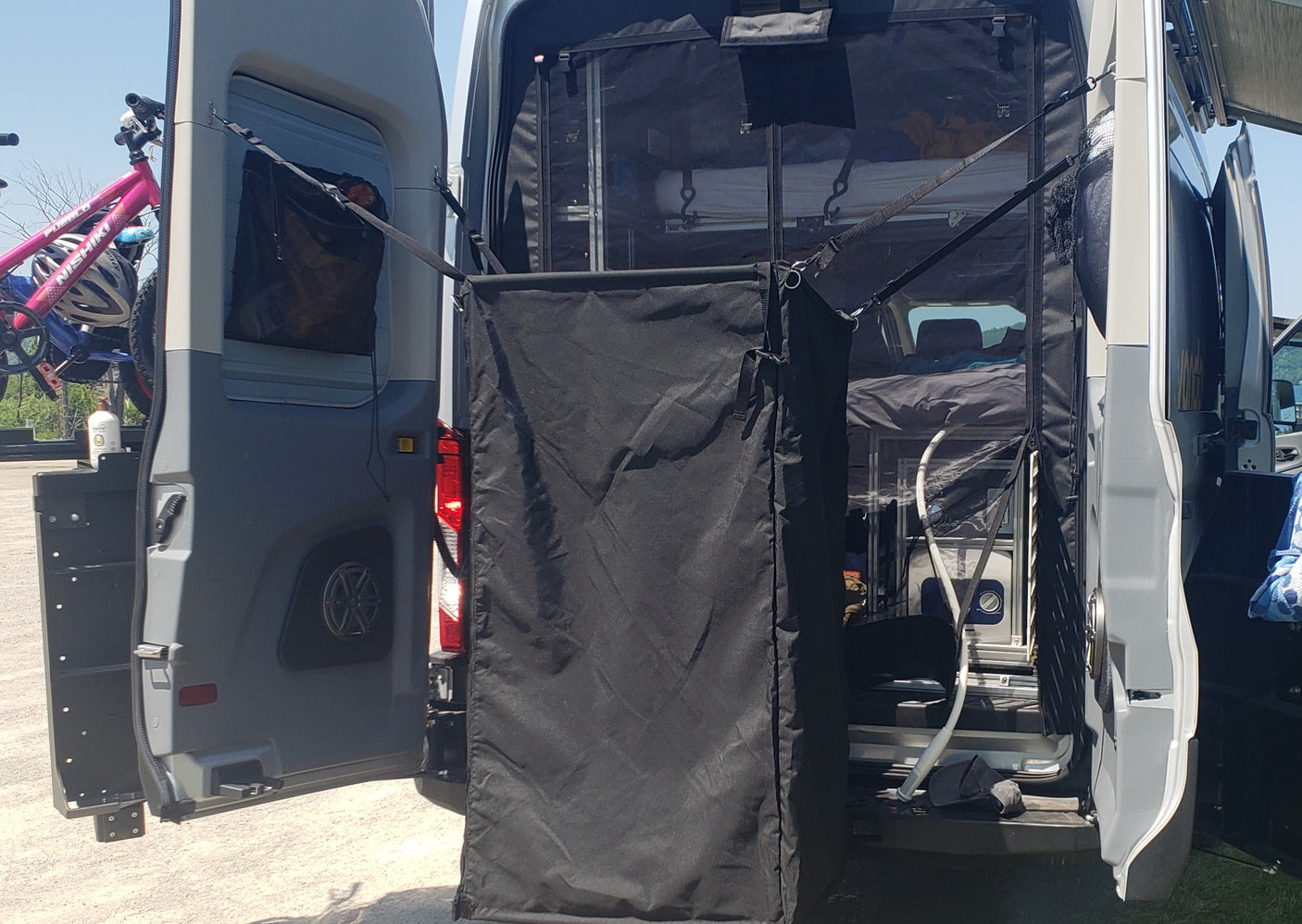 RV rental setup: rear doors open showing a bike rack, interior bed/storage, and an outdoor privacy tent deployed.