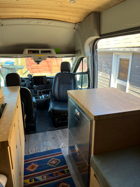 Spacious RV rental interior featuring warm wood cabinetry, built-in fridge, and a clear view to the driver's cockpit.