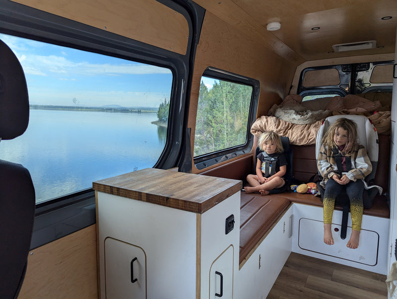 Two children relax in a spacious RV rental, enjoying scenic lake and forest views from inside their camper van. — photo 17
