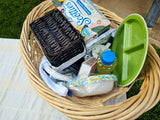 Wicker basket packed with RV rental trip essentials: Scotties tissues, paper bowls, a green plate, and other picnic supplies.