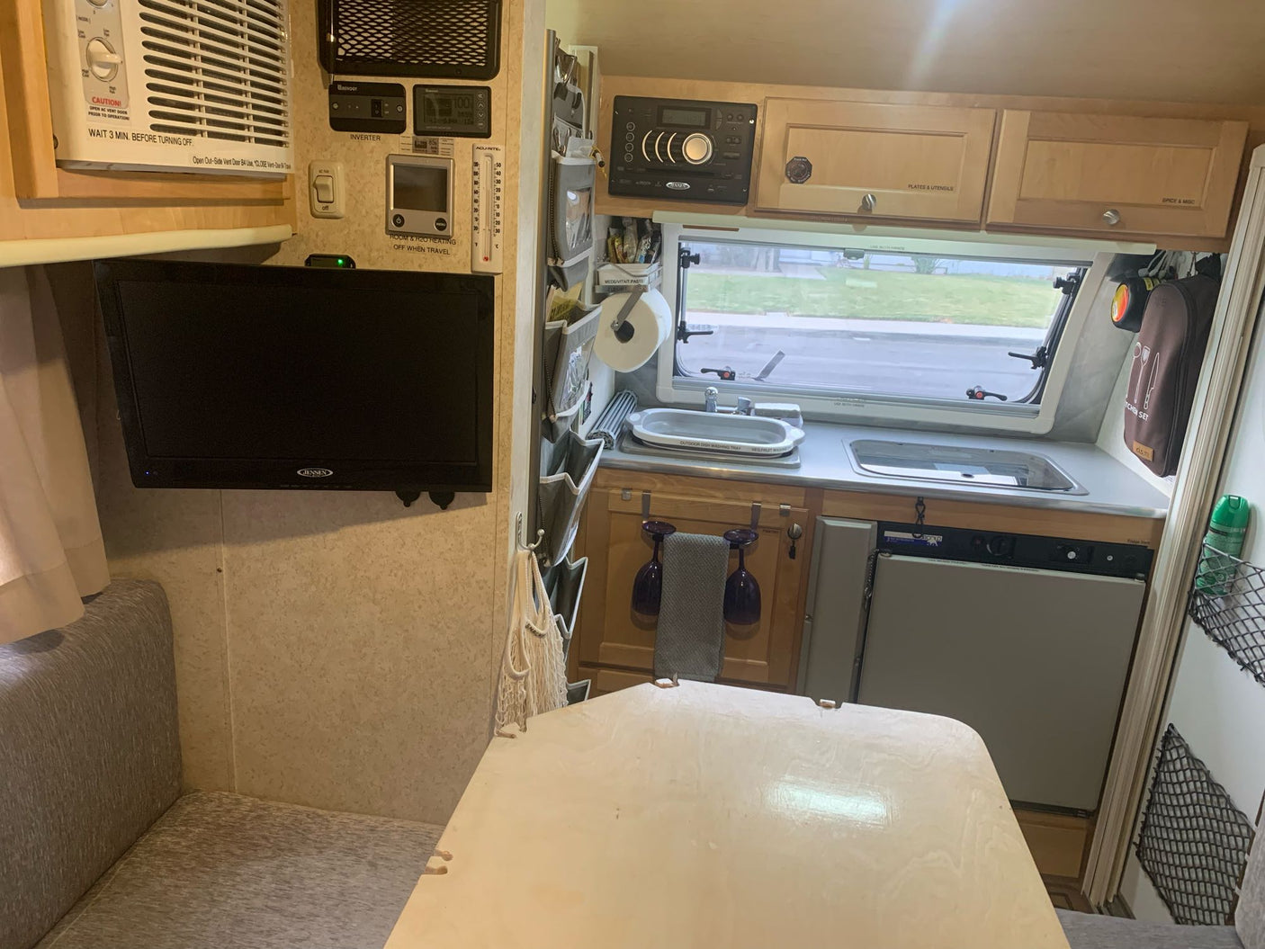 This RV rental's well-equipped interior features a compact kitchen, dining table, TV, and AC unit for comfortable travel.