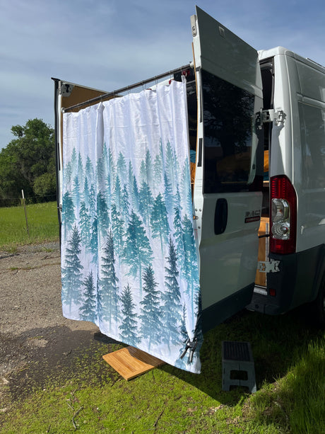 RV rental: Outdoor shower setup with a pine forest curtain, wooden mat, and step stool at the rear of a white camper van.