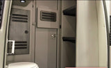 An RV rental's compact interior: showing a toilet, a light-colored wood-paneled wall with vents, and open storage shelves.