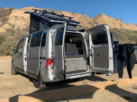 Gray pop-top camper van, perfect RV rental, open to sandy adventure. Wetsuits dry by the rear, ready for coastal fun.