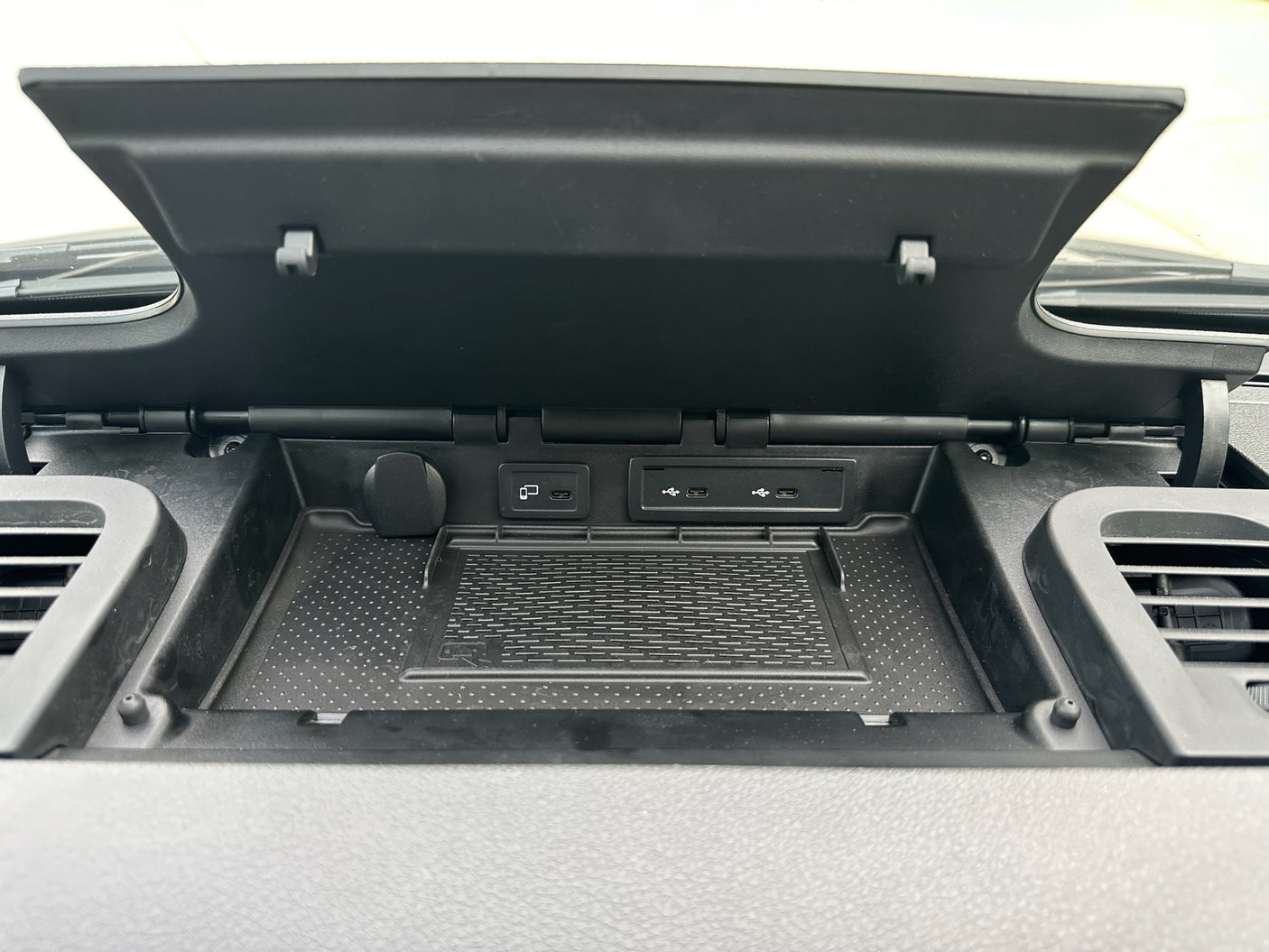 RV rental: View of an open dashboard compartment with a 12V outlet, USB-C ports, and wireless charging pad.