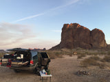 Car camping SUV setup, an RV rental alternative, in a stunning desert landscape with rugged rock formations at sunset.