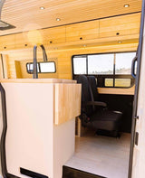 Spacious RV rental interior featuring a modern kitchen area with sink, light wood accents, and comfortable passenger seating.