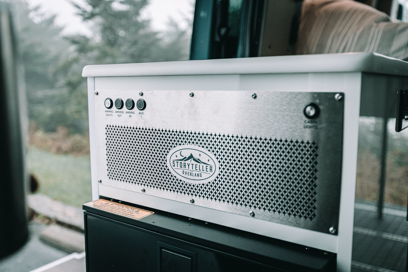Inside an RV rental: Storyteller Overland control panel features awning, auxiliary, and cabin light controls, plus a refrigerator.