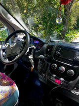 Inside a cozy rv rental, showcasing the dashboard, steering wheel, and a floral seat, with green trees seen through the windshield.