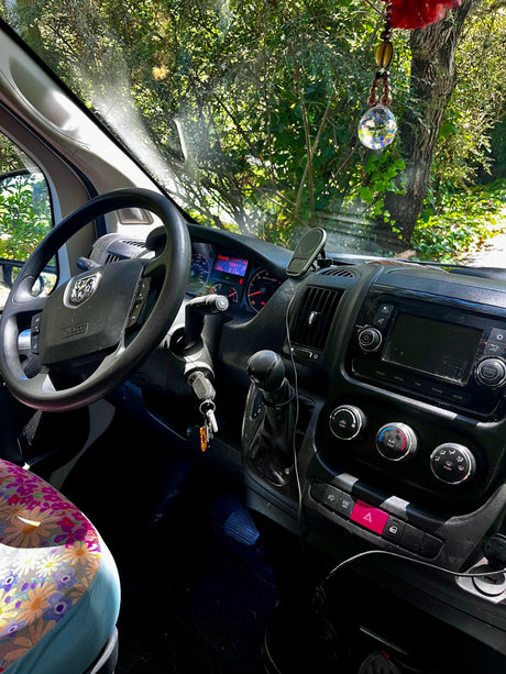 Inside a cozy rv rental, showcasing the dashboard, steering wheel, and a floral seat, with green trees seen through the windshield.