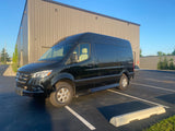 A sleek black Mercedes Sprinter van, perfect for RV rental getaways, parked by a modern building on a sunny day.