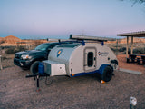 Teardrop RV rental camper and truck at a desert campsite, featuring hills and a picnic area.