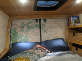 Cozy RV rental bedroom with maps on the back doors, a comfy bed, wooden ceiling, and travel books and storage baskets nearby.