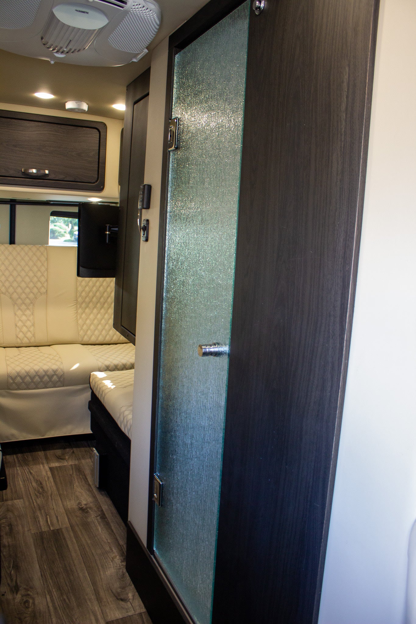 RV rental interior: modern frosted glass door, wood-look floor, and comfortable quilted seating, ideal for mobile living.