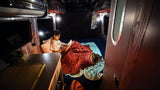 A person reads in a cozy RV rental bed with their dog, illuminated by warm lights, for a perfect night.