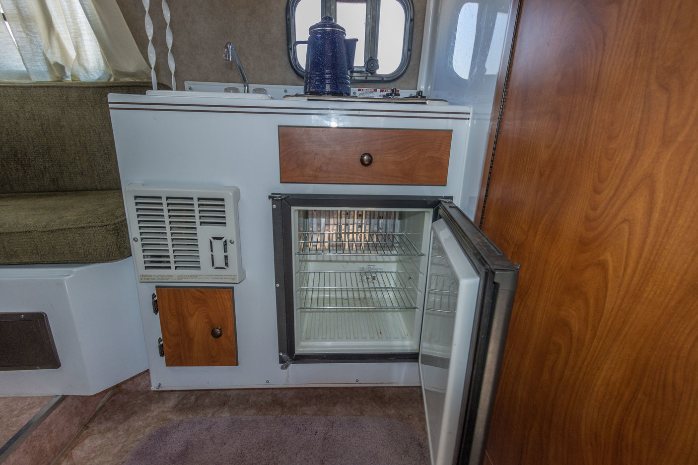 Inside an RV rental: compact kitchen with sink, open fridge, and heater, plus cozy seating by the window.