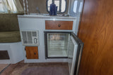 Inside an RV rental: compact kitchen with sink, open fridge, and heater, plus cozy seating by the window.