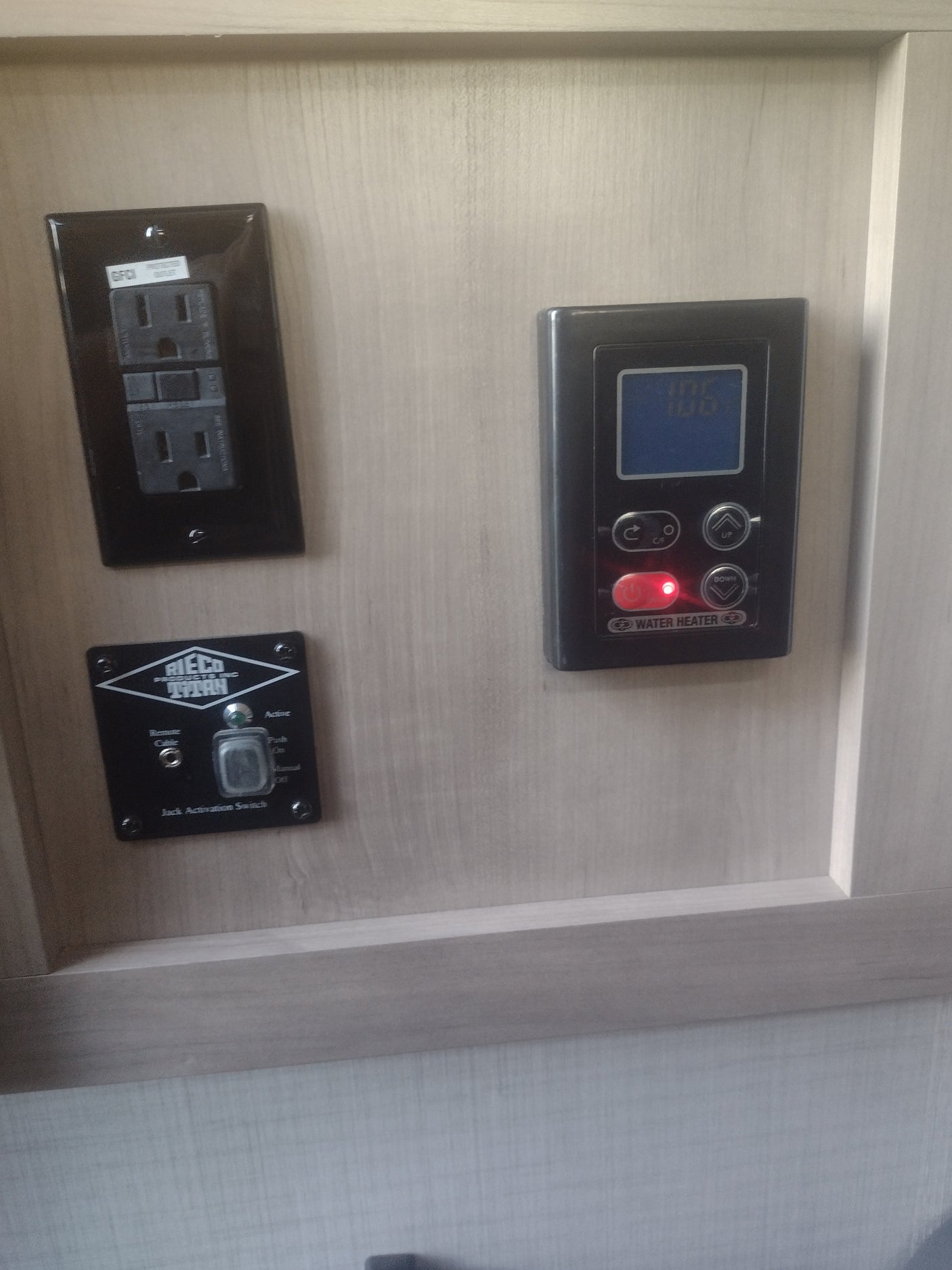 RV rental interior showing essential controls: GFCI outlet, water heater panel, and Rieco Titan jack switch.
