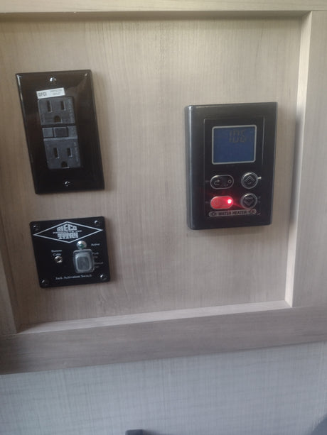 RV rental interior showing essential controls: GFCI outlet, water heater panel, and Rieco Titan jack switch.