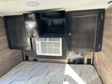Inside an rv rental: Cozy sleeping area with a bed, mounted TV, Frigidaire AC unit, dark wood cabinets, and outlets.